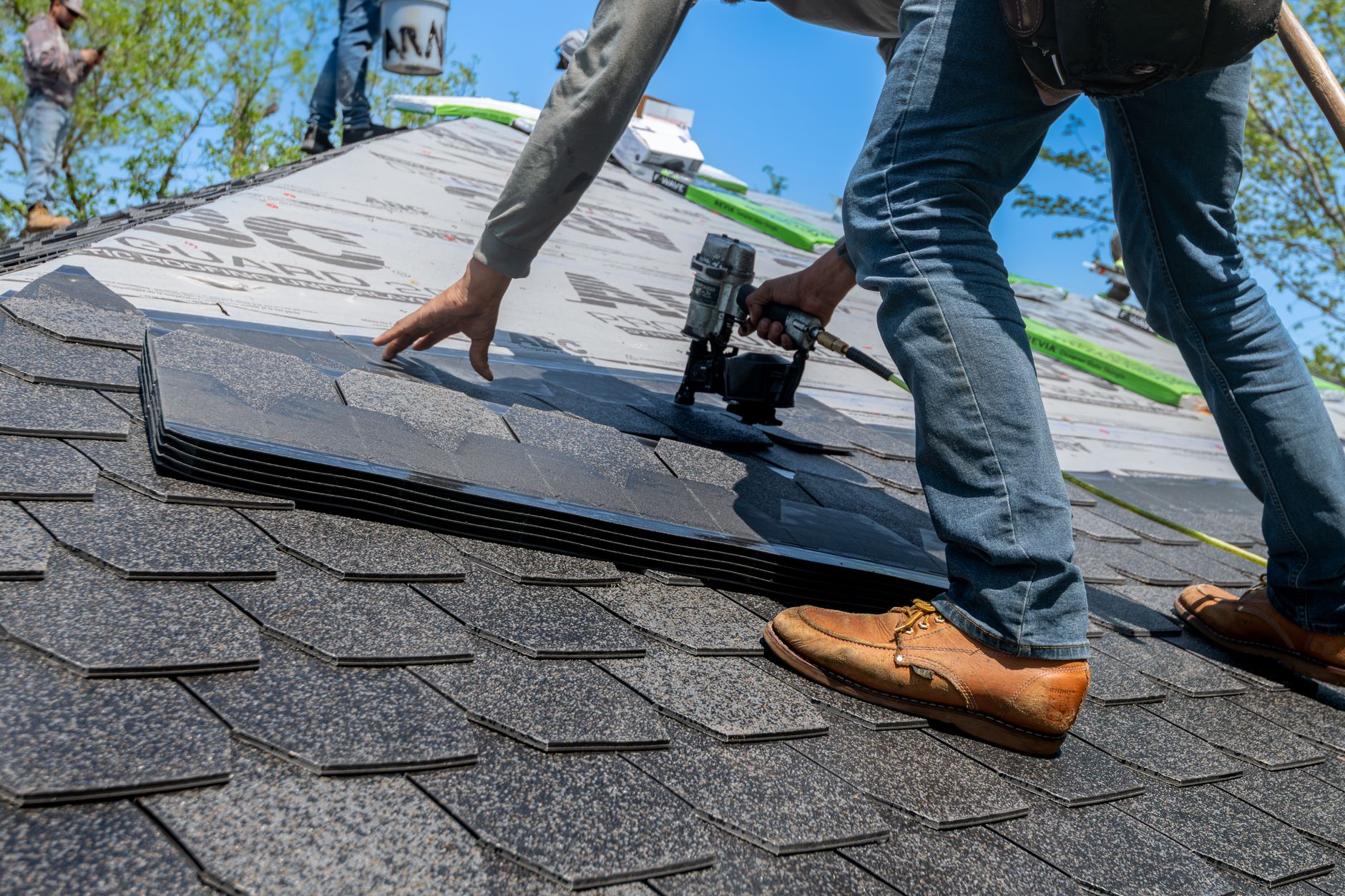 Roofer nailing new asphalt shingles onto a roof with a nail gun.